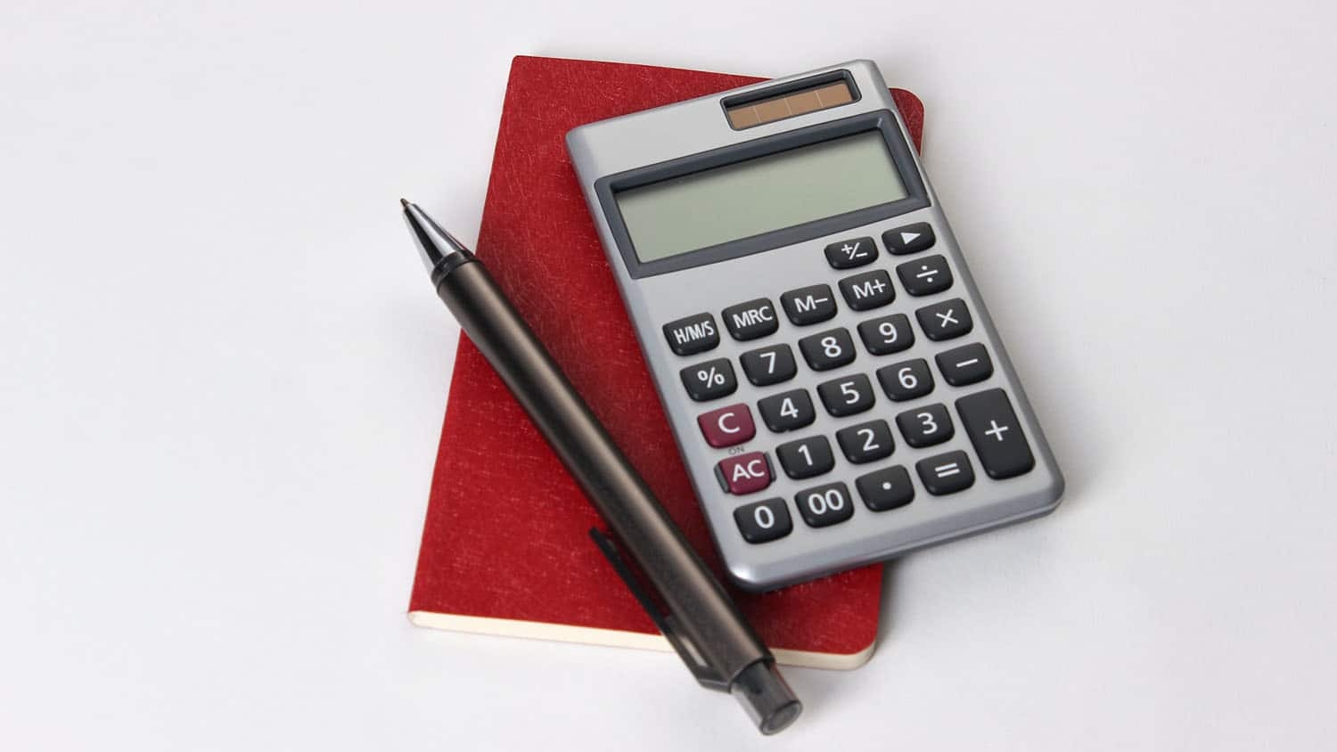 photo shows a notebook, calculator and pen lying on a white surface