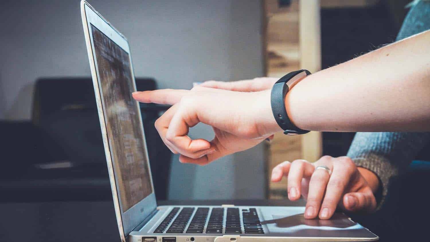 the hands of two different people hover over a laptop, as if one person is explaining something to another person